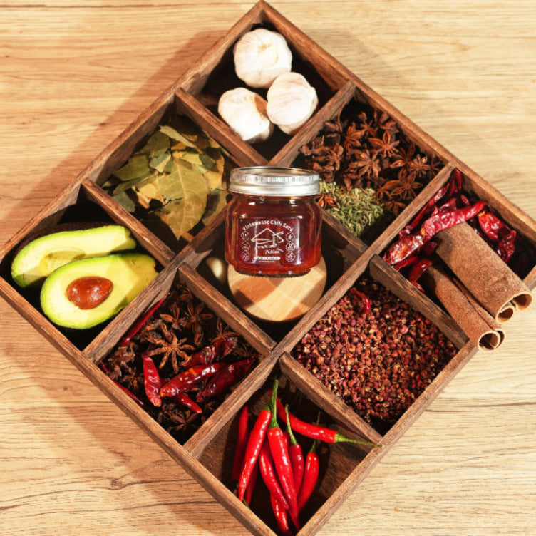 Wooden box with compartments containing spices, herbs, and a jar of jam on a wooden surface.