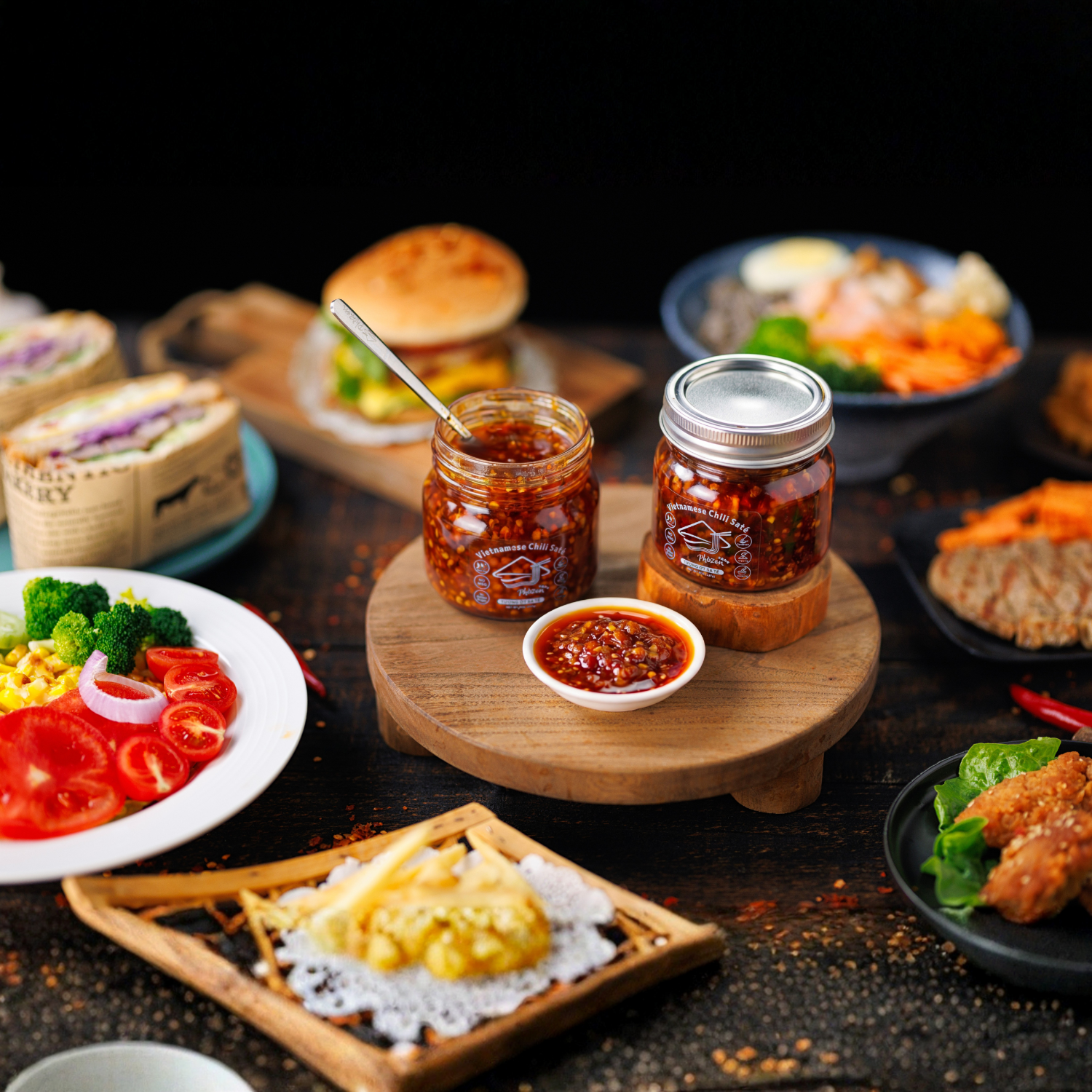 Jars of condiments on a wooden board with various food items in the background