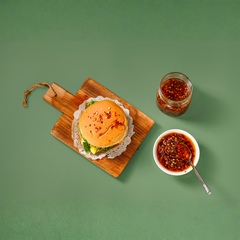 Hamburger on a wooden board with two bowls of sauce on a green background