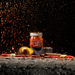Jar of hot sauce with chili peppers and spices on a dark surface with sparks.