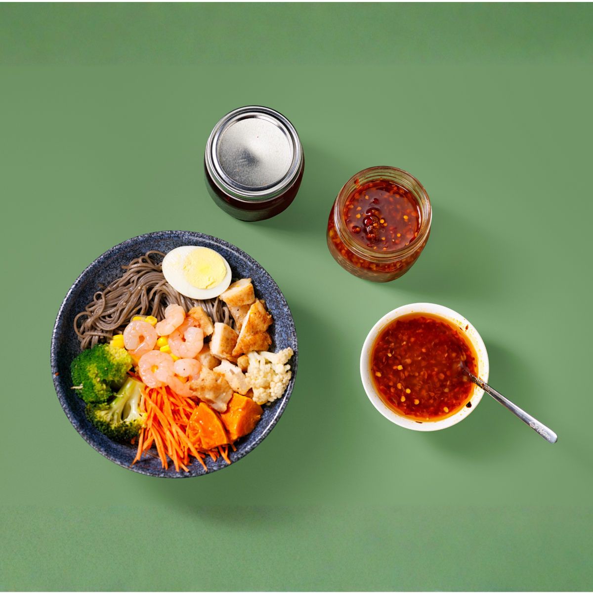 Bowl of noodles with vegetables and a side of sauce on a green background